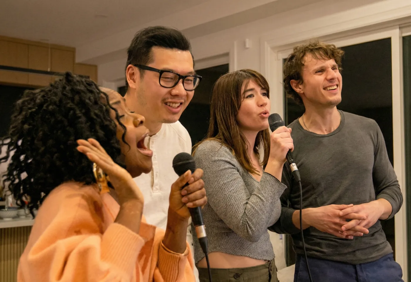 Four friends singing together, two sharing microphones