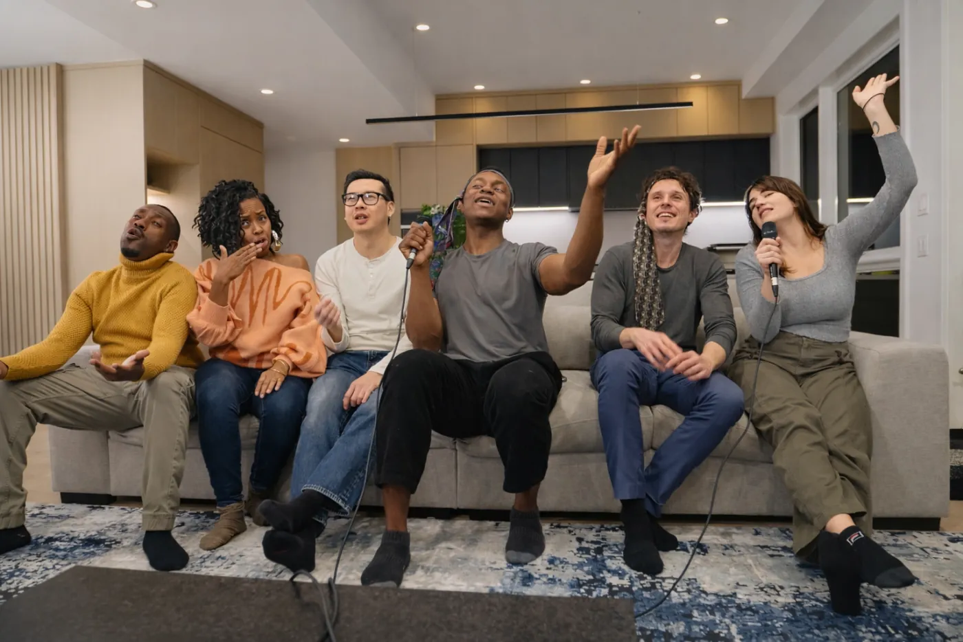 Six friends singing along from a couch, one holding a microphone