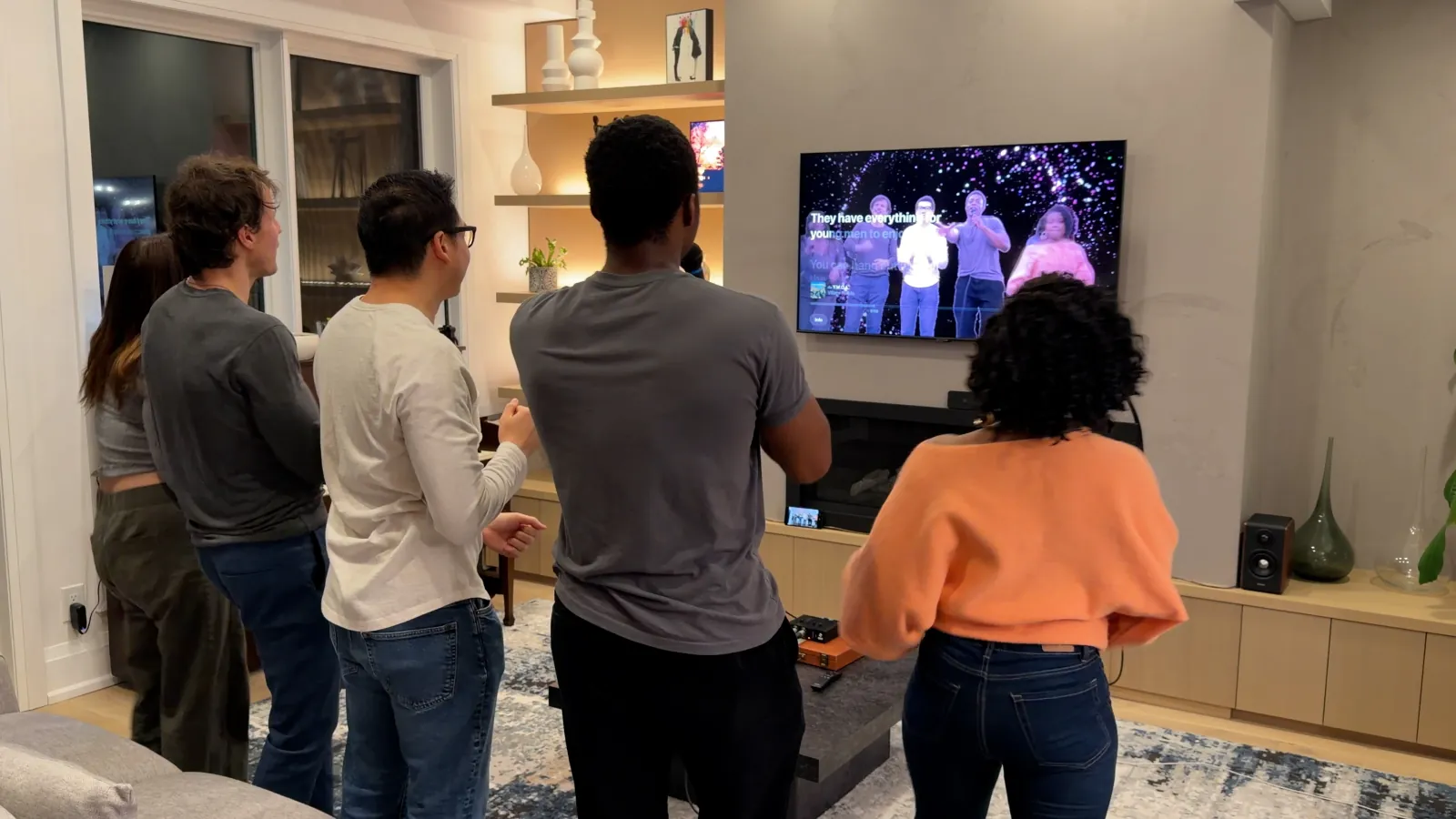 Friends watching karaoke lyrics on a wall-mounted television in a living room